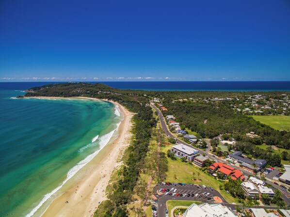 An aerial view of a coastal area with a beach, a road, and residential buildings.