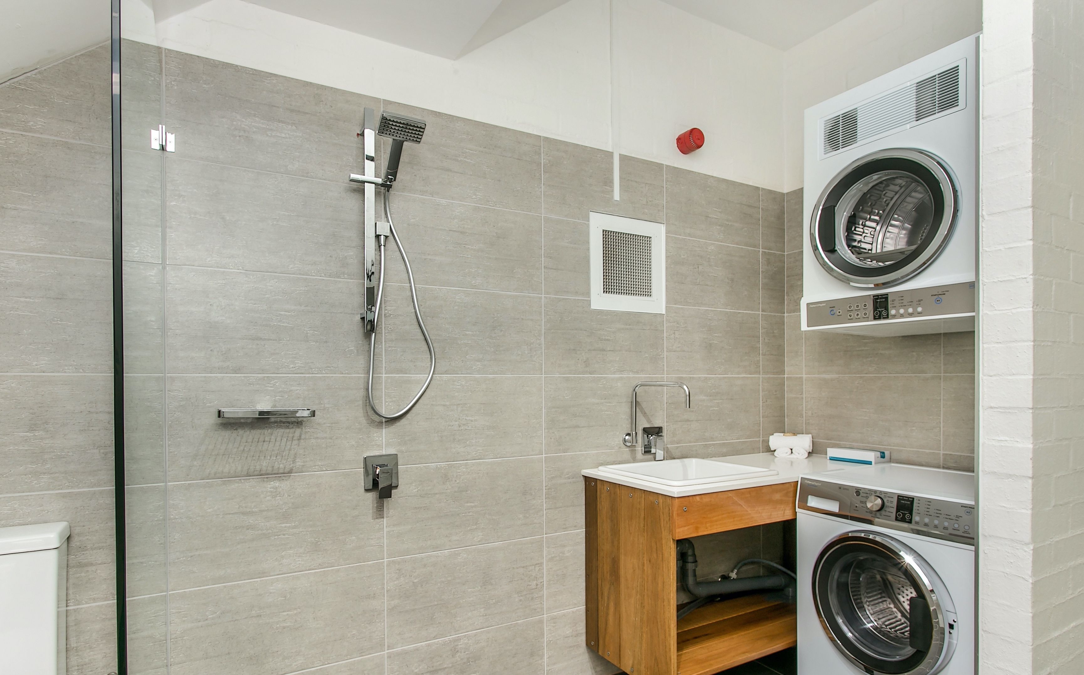 A modern bathroom with a glass shower enclosure, a built-in sink, and a stacked washer and dryer unit.
