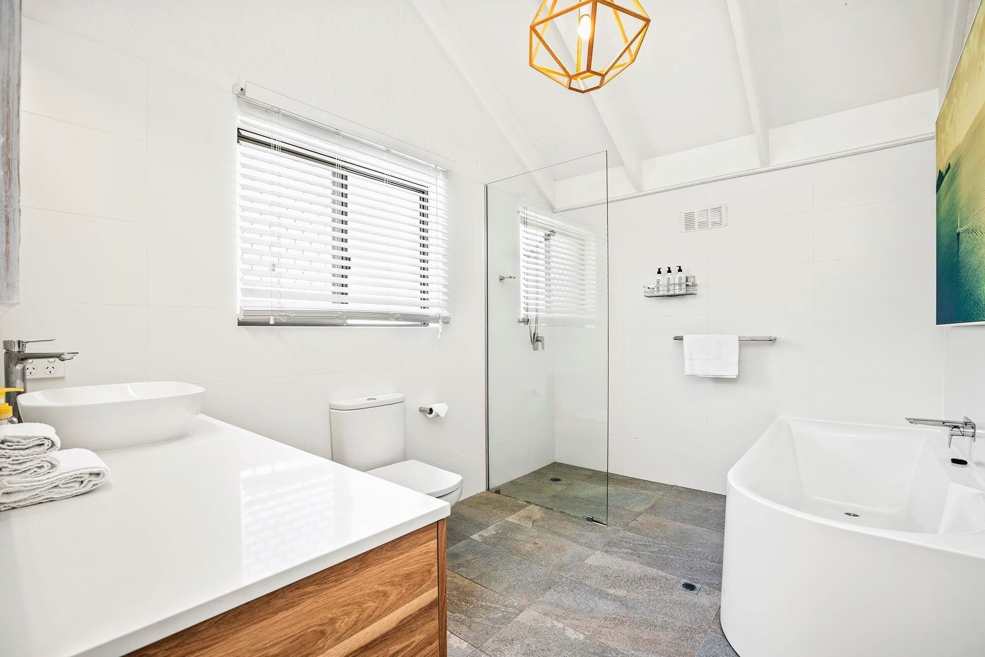 Un baño moderno con una bañera independiente, ducha con mampara de vidrio y tocador con armario de madera.