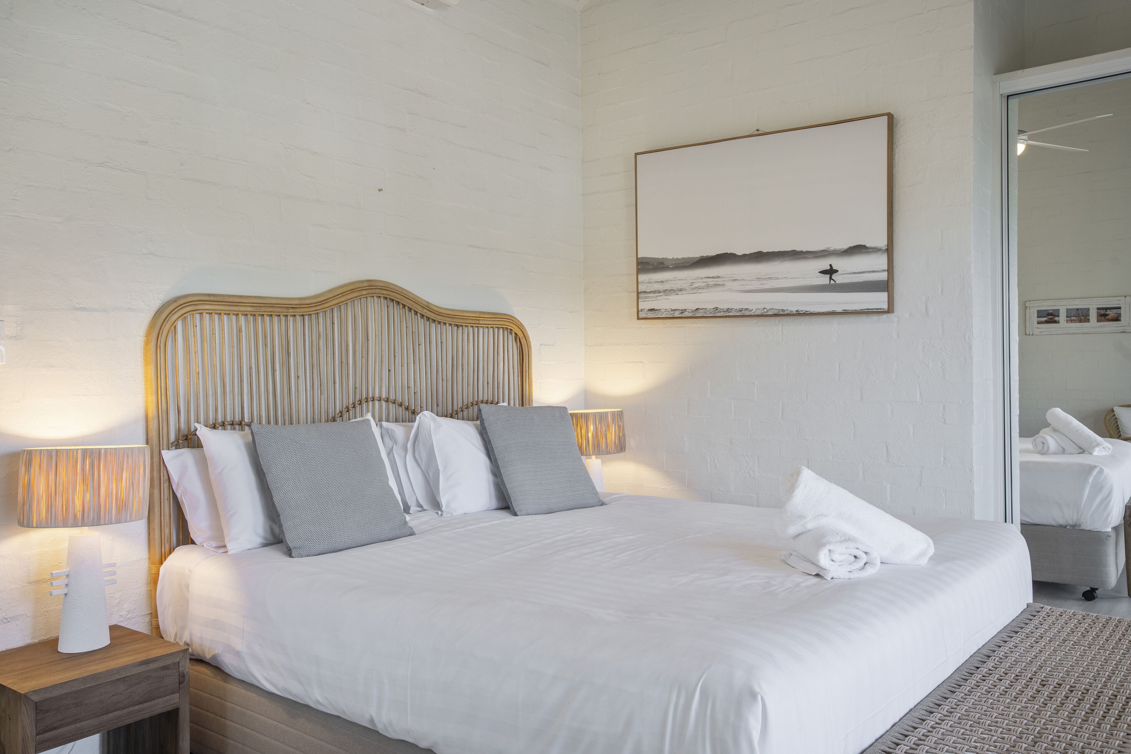 A neatly made bed with a wooden headboard, a bedside lamp, and a framed picture on the wall.