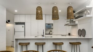 Une cuisine moderne avec des meubles blancs, un îlot central doté de tabourets de bar et des luminaires suspendus en fibres tressées.