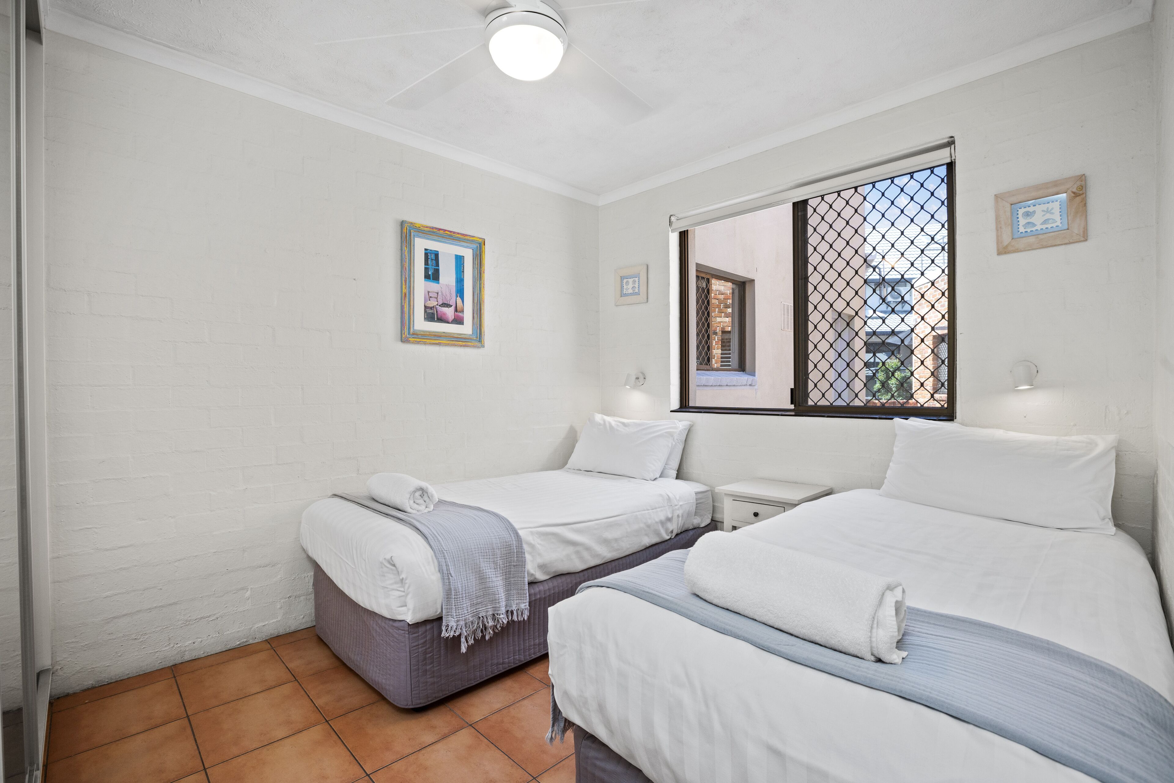 A room with two beds, white walls, a window with a view, and a ceiling fan.