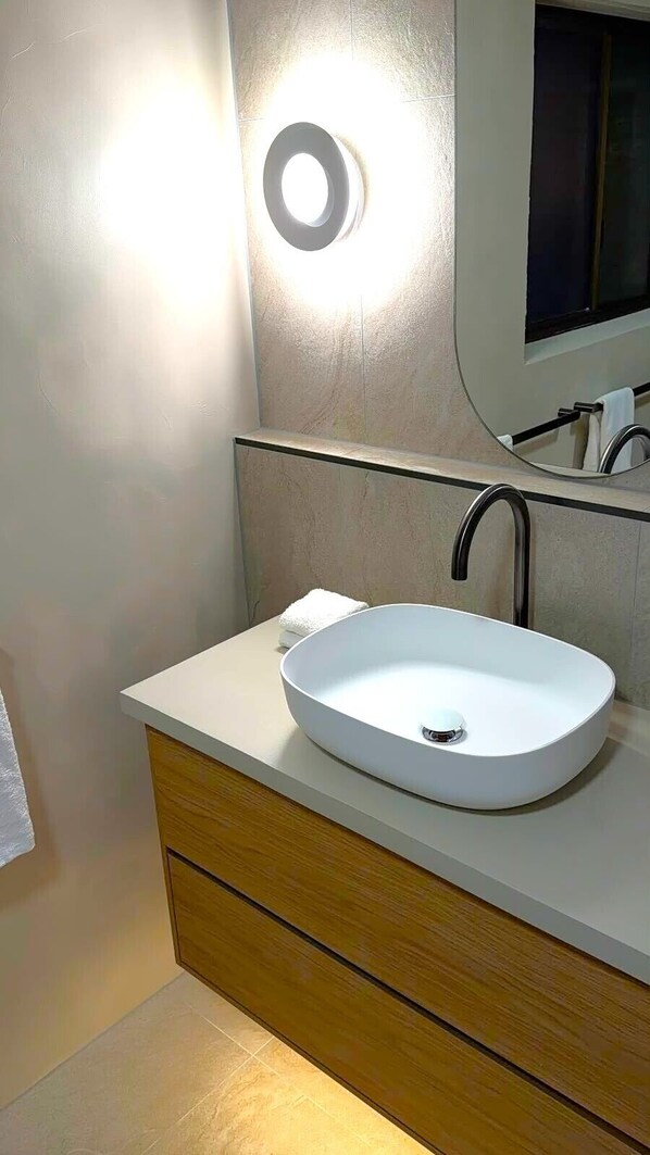 Un baño con un lavamanos blanco, un espejo y una lámpara en la pared.