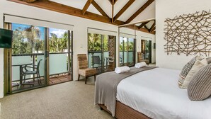 Une chambre dotée d’un grand lit, d’un coin salon avec un fauteuil et d’un balcon avec une porte vitrée.