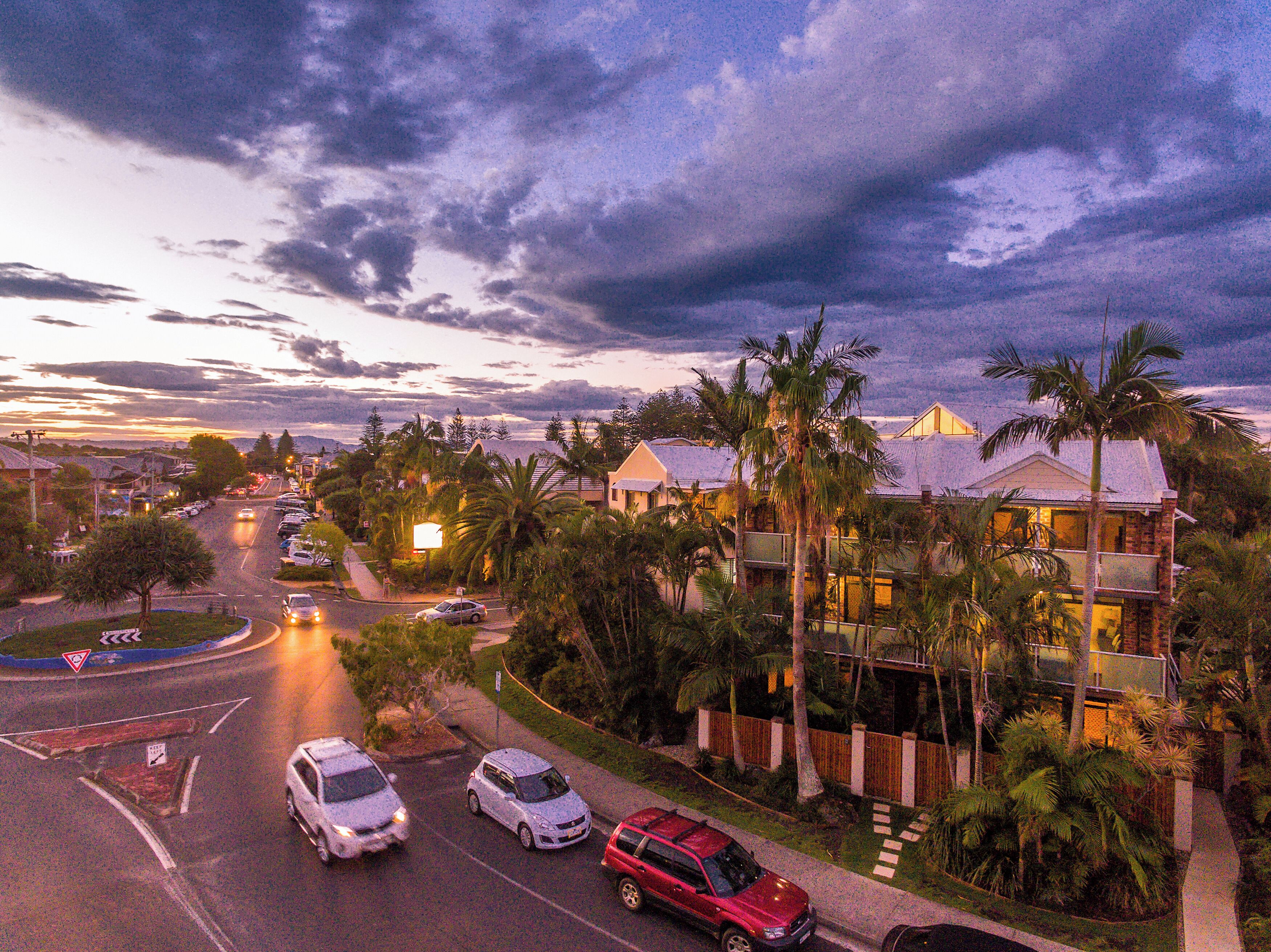 A residential area with houses, palm trees, and a road with cars.