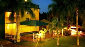 A two-story building with a covered patio area, surrounded by palm trees and a well-lit outdoor space. - Sky View Units (Bowen)
