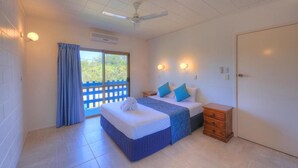 A bedroom with two beds, a ceiling fan, a small wooden nightstand, and a sliding glass door leading to a balcony. - Sky View Units (Bowen)