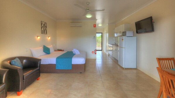 A hotel room with a bed, a sofa, a TV, a kitchen area, and a dining table.
