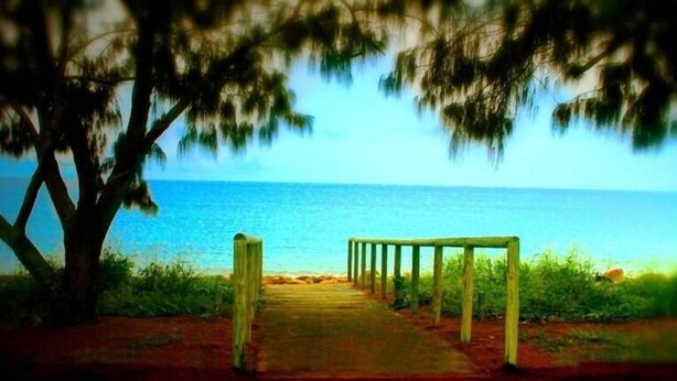 A pathway leading to a beach with a wooden structure in the middle. - Sky View Units (Bowen)