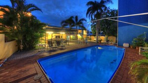 A swimming pool with a wooden deck, lounge chairs, and a covered patio area with tables and chairs. - Sky View Units (Bowen)