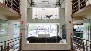 A modern hotel lobby with a central seating area, glass railings, and a view of the street outside. - Hotel Velario (Tijuana)