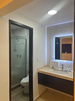 A modern bathroom with a glass shower enclosure, a toilet, a sink with a mirror, and a towel on the counter.
