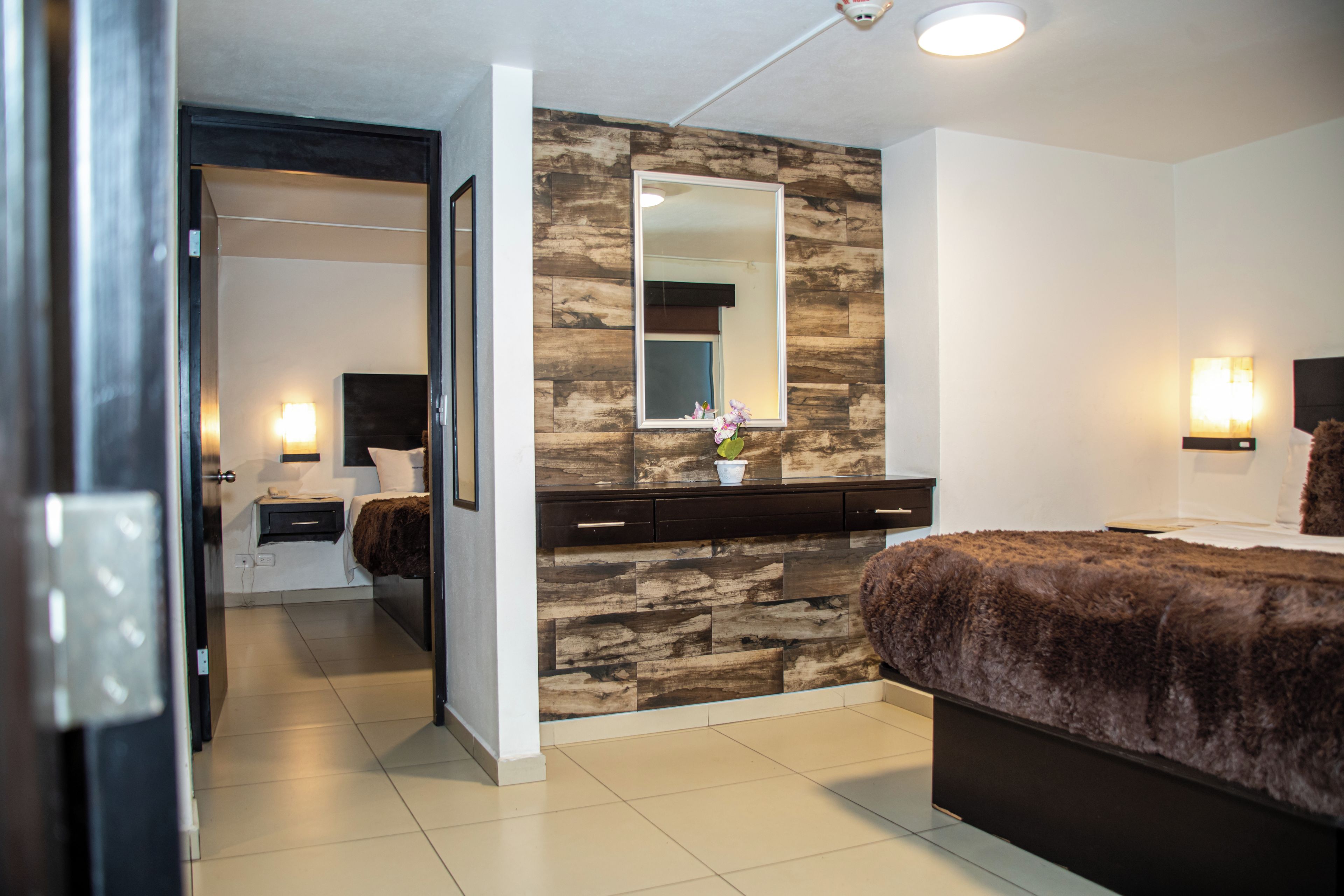Ein modernes Schlafzimmer mit Steinwand, großem Spiegel, Bett, Kommode und Nachttisch.