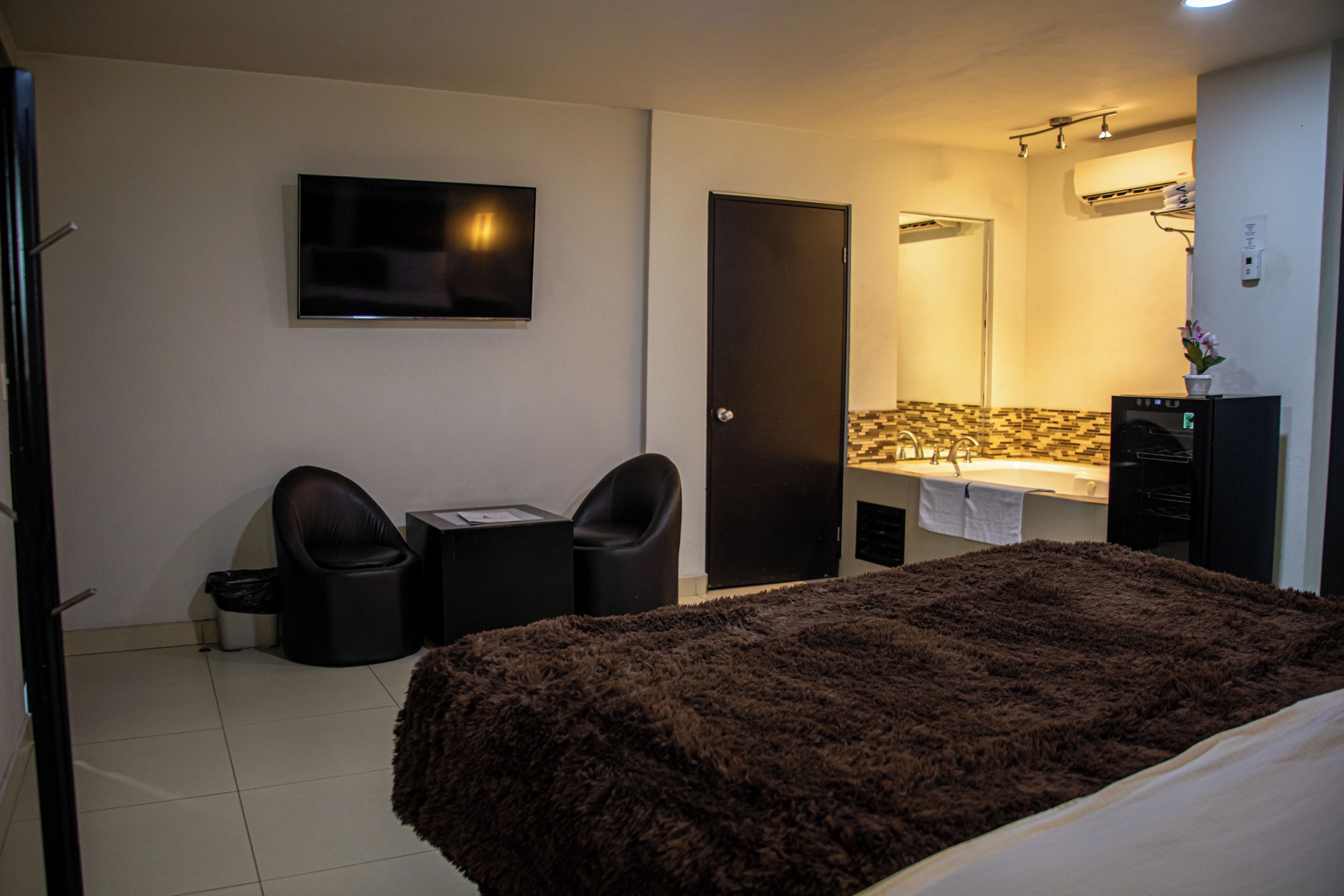 Ein Hotelzimmer mit einem Bett, einem Schreibtisch, zwei Stühlen, einem Fernseher, einer Tür und einem Badezimmer mit Waschbecken und Spiegel.