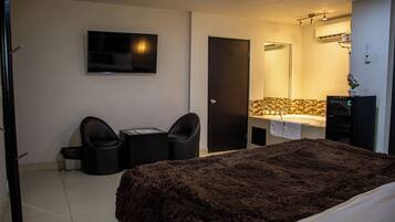 Ein Hotelzimmer mit einem Bett, einem Schreibtisch, zwei Stühlen, einem Fernseher, einer Tür und einem Badezimmer mit Waschbecken und Spiegel.