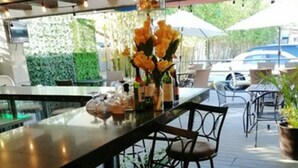 A bar area with stools, a glass counter, and a vase with flowers. - Hotel Velario (Tijuana)