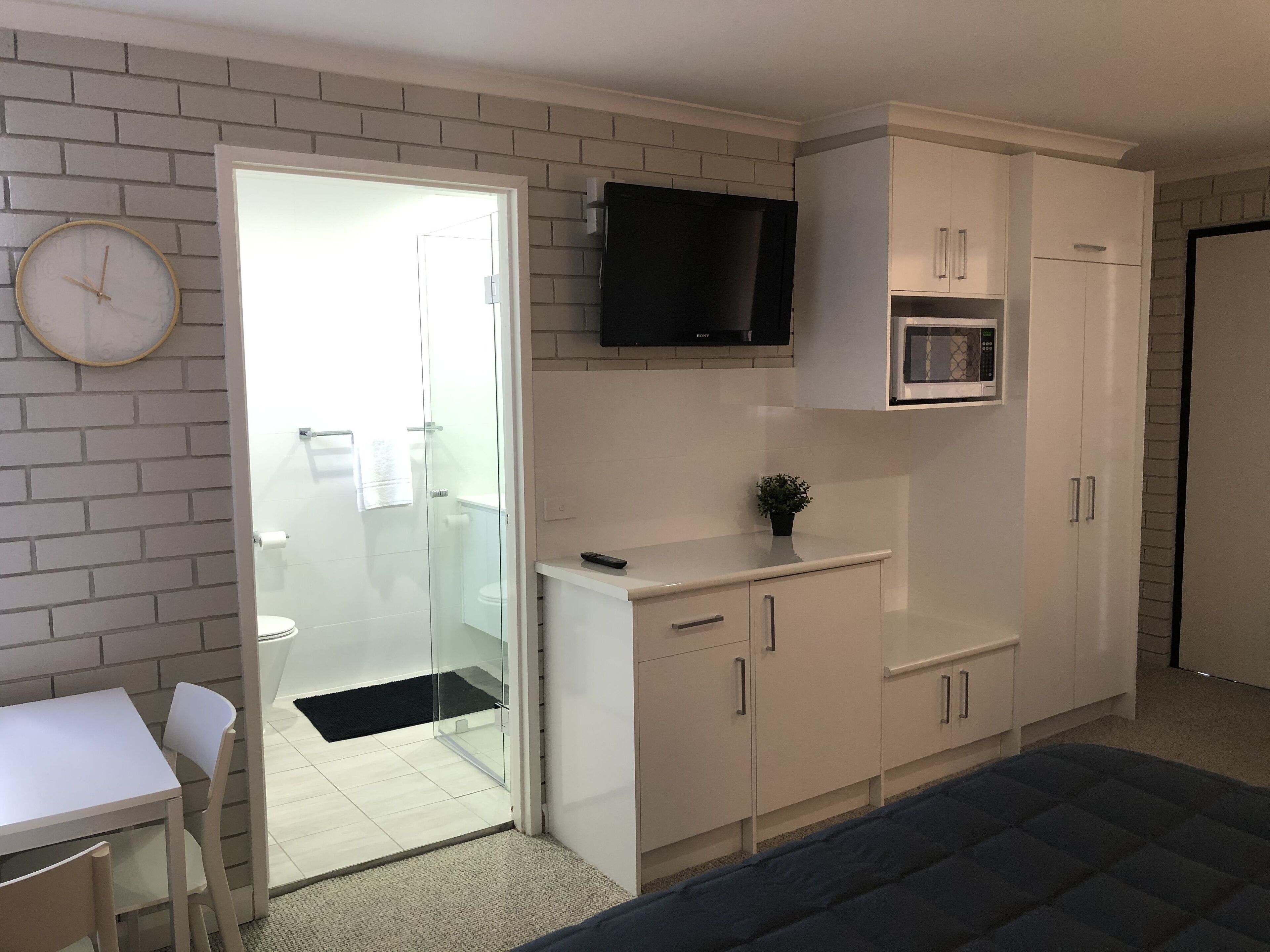 A compact kitchen with white cabinets, a microwave, a TV, and a dining area with a table and chairs.