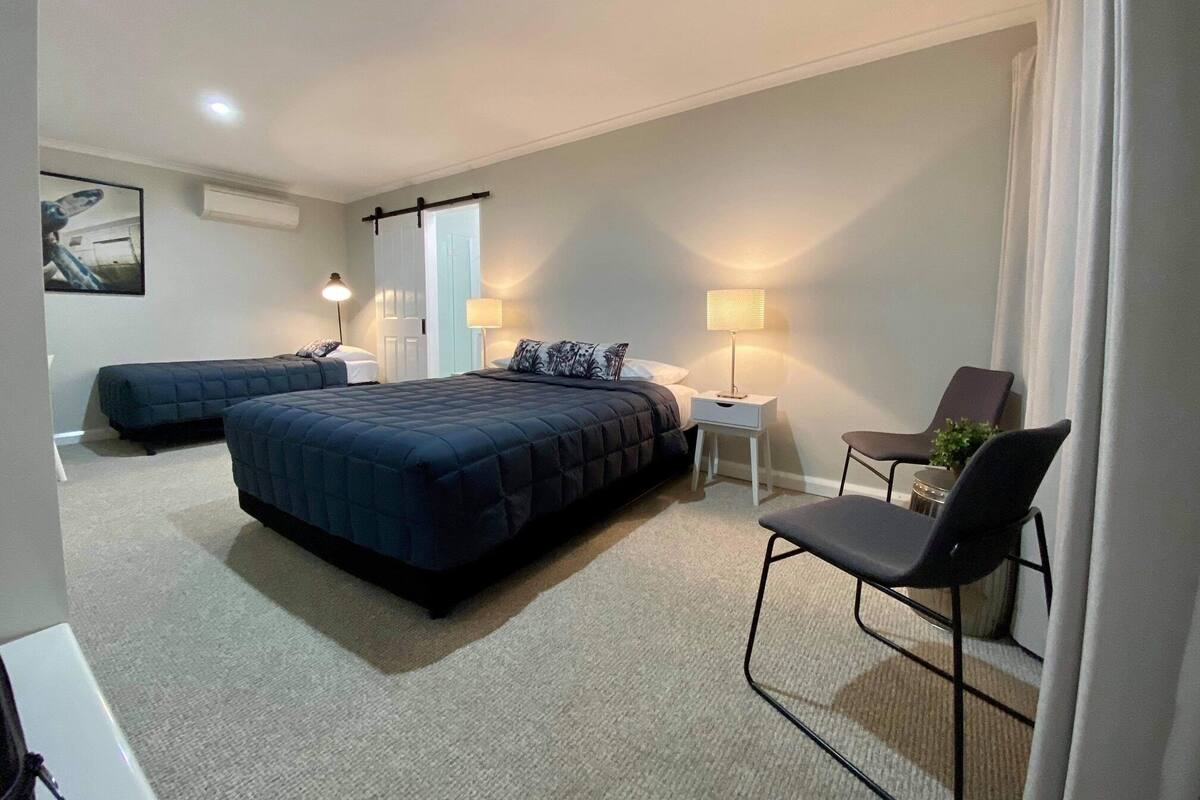 A modern bedroom with two beds, a desk, a chair, and a lamp.