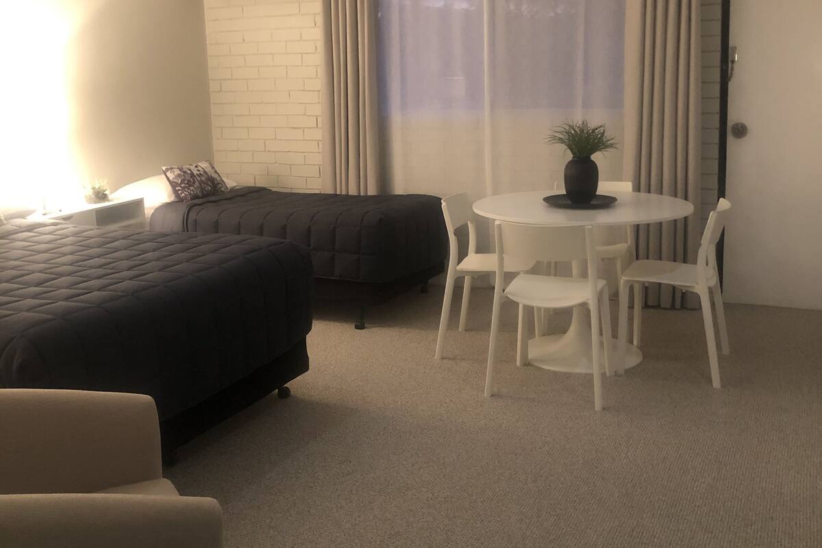 A bedroom with a bed, a small round table with chairs, a sofa, and a potted plant.
