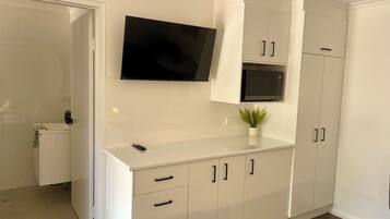 A modern kitchen with white cabinetry, a flat-screen TV mounted above the counter, and a microwave.