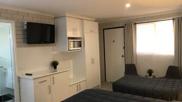A compact room with a kitchenette, a TV, two beds, and a door leading to a bathroom.
