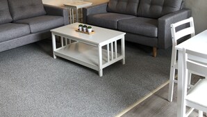 A modern living room with two grey sofas, a white coffee table with plants, a lamp, and a macrame wall hanging.