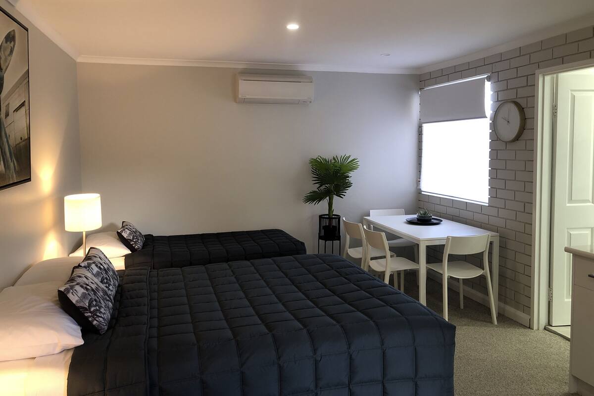 A bedroom with a bed, bedside table, lamp, and a small desk with chairs.