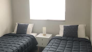 Un dormitorio con dos camas, una mesita de noche y una ventana.