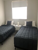 Un dormitorio con dos camas, una mesita de noche y una ventana.