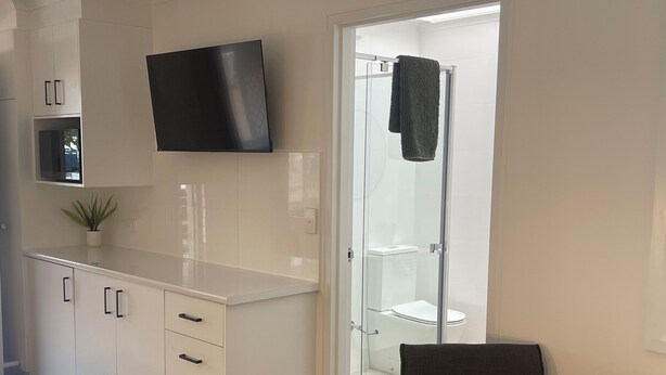 A modern kitchen with white cabinetry, a flat-screen TV, and a glass door leading to a bathroom.