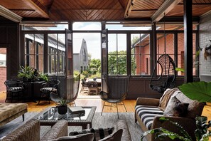 Eine großzügige Terrasse mit Glaswand, Korbmöbeln und einer Hängemattenstuhl.