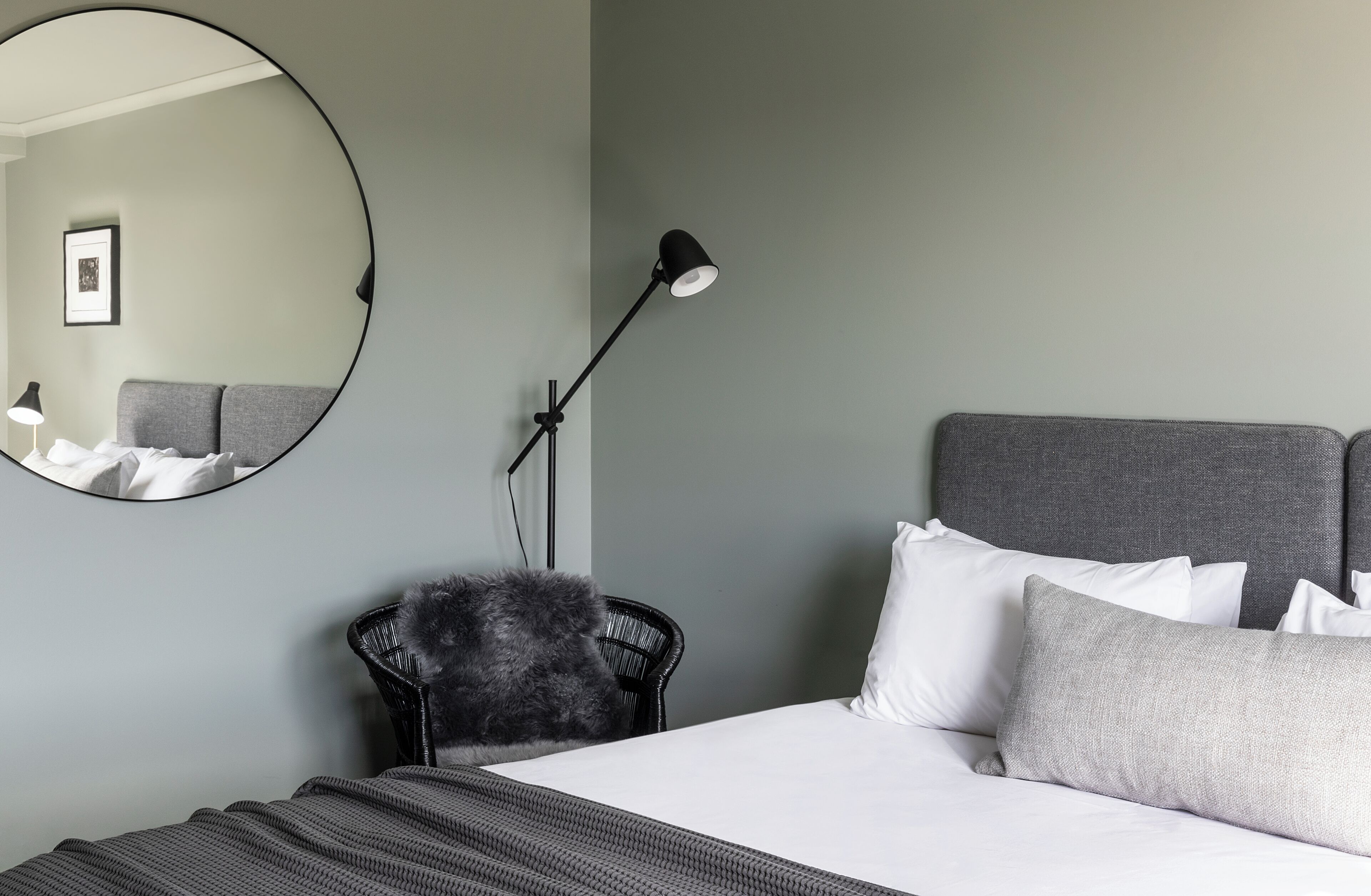 Ein ordentlich eingerichtetes Schlafzimmer mit einem Bett, einem runden Spiegel, einer Stehlampe und einem Sessel.