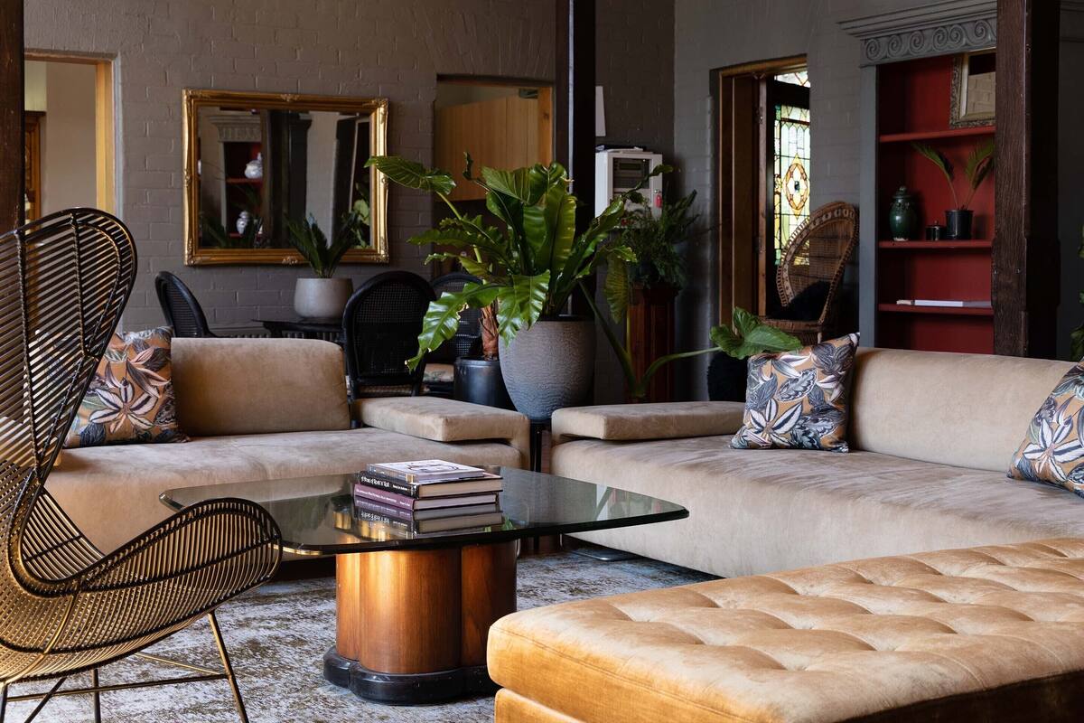 A modern living room with a sofa, a glass coffee table, and a chair. There are plants and a bookshelf in the background.