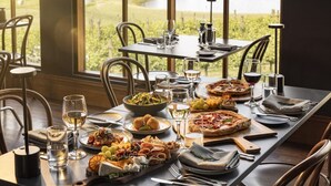 A dining table set for a meal with various dishes, glasses, and cutlery, overlooking a vineyard. - Cleveland Estate (Lancefield)