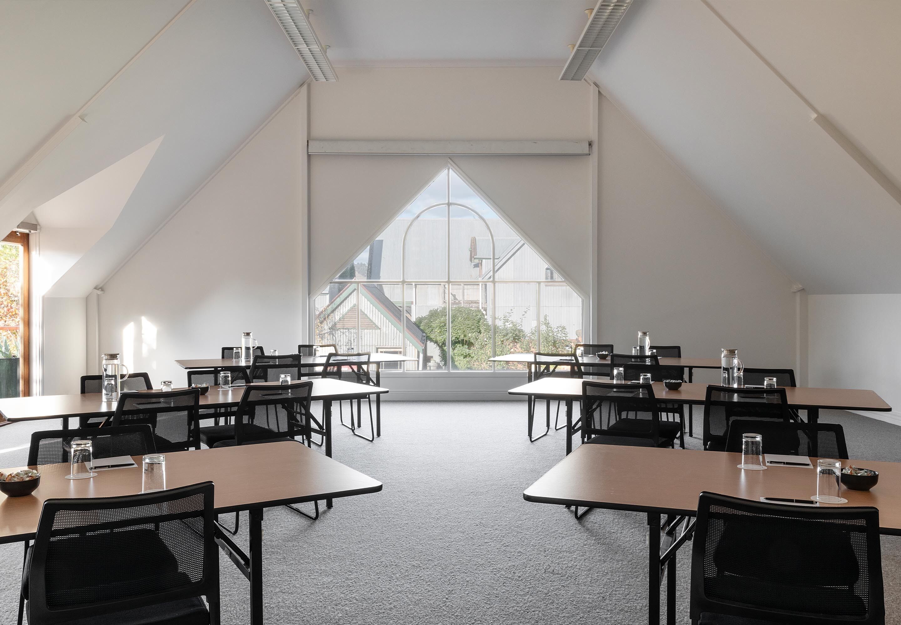 Un salón de conferencias con mesas y sillas, ventanas amplias y vistas a edificios.
