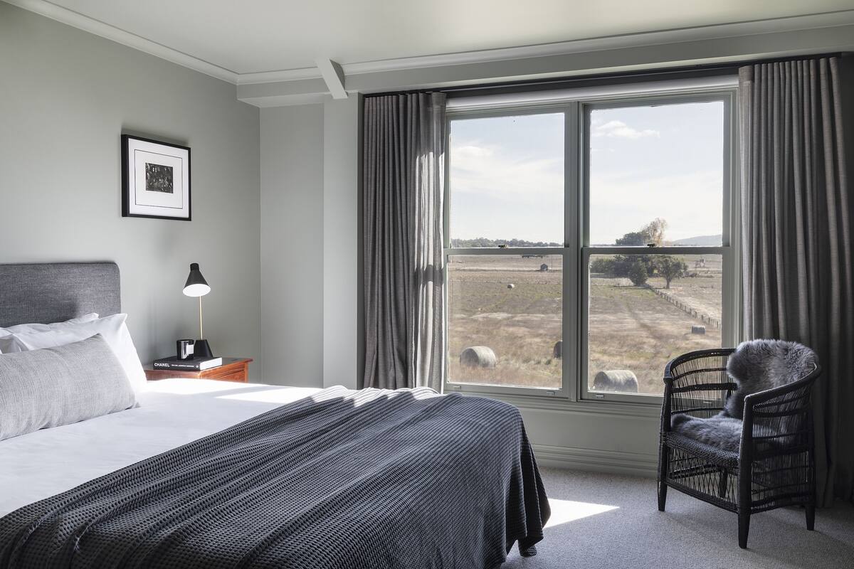 A hotel room with a large bed, a chair by the window, and a picture on the wall.