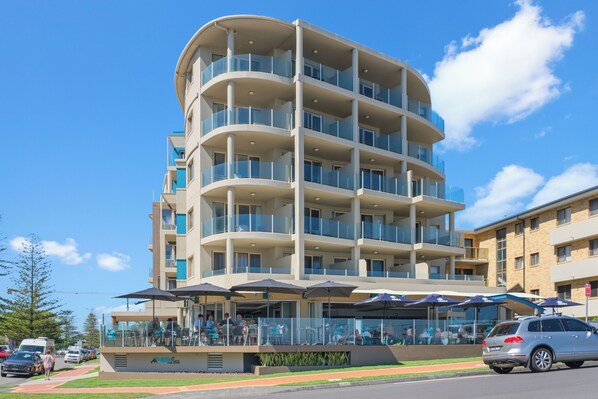 Un hotel de varios pisos con balcones, mobiliario exterior y cielo despejado.