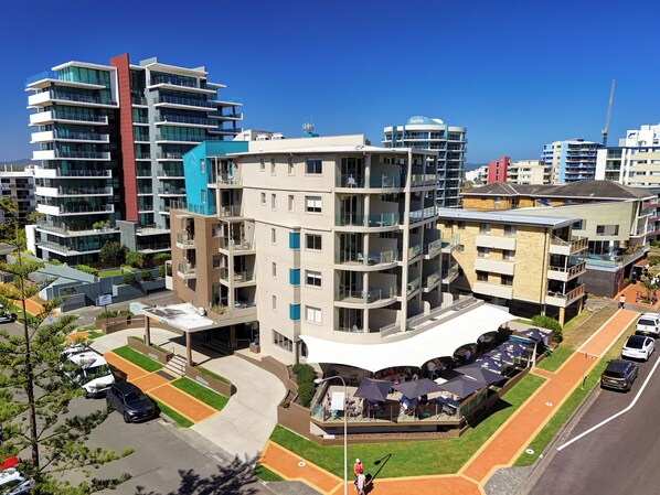 A multi-story building with balconies, a parking area, and a restaurant with outdoor seating. - The Dorsal Boutique Hotel (Forster)