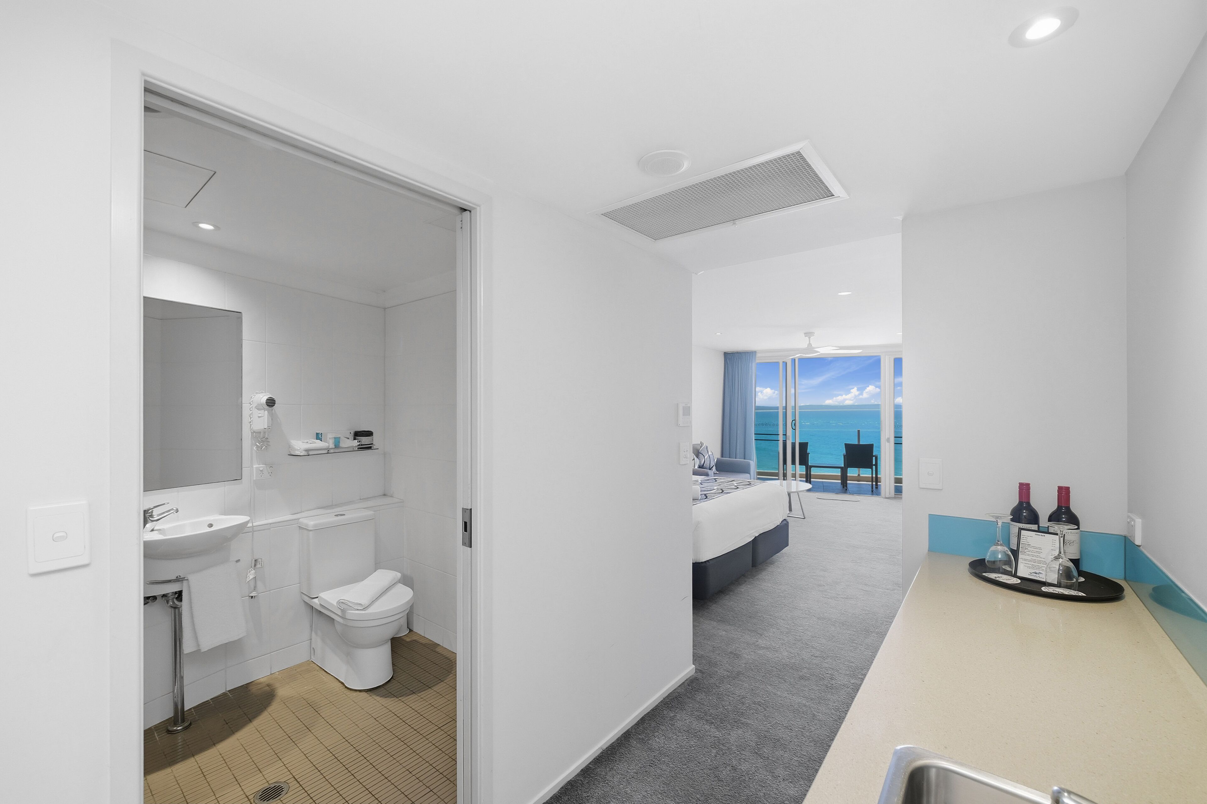 Una habitación de hotel moderna con baño, cama, vista al mar y zona de desayunos.