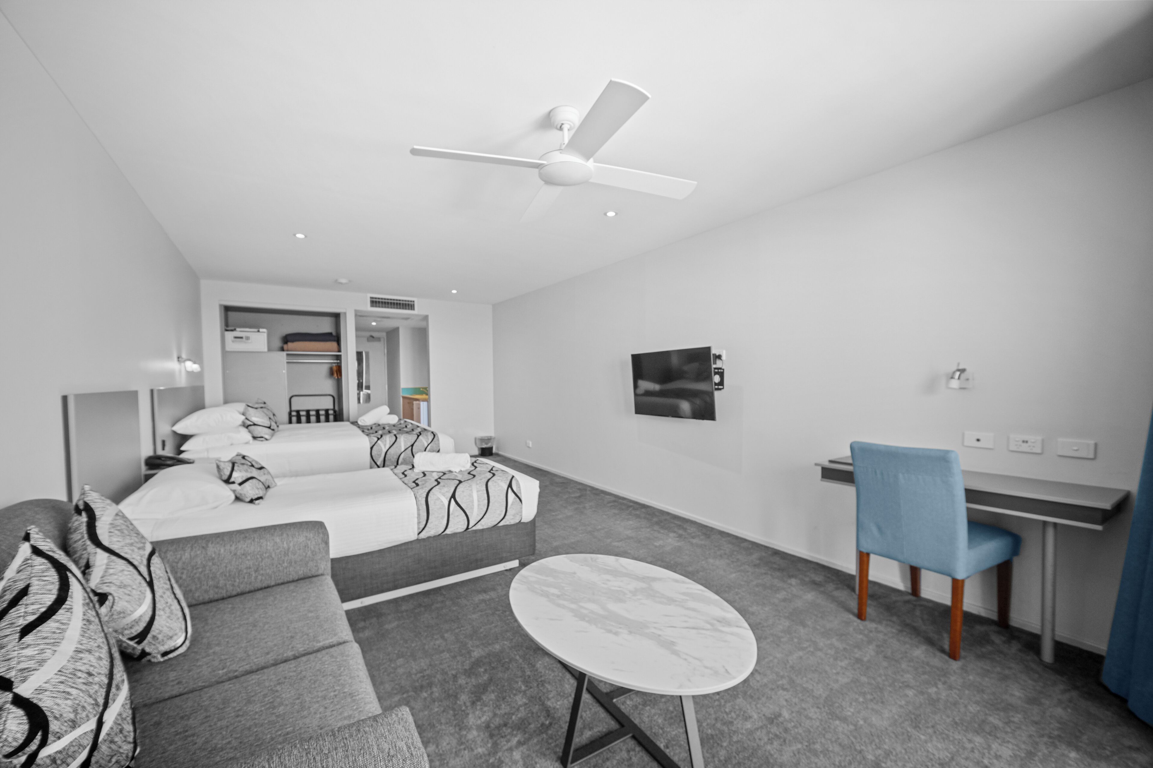 A modern hotel room with a bed, a sofa, a desk, and a ceiling fan.