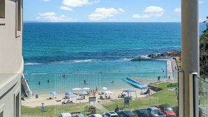 Une vue d’une plage avec une piscine, des parasols et des voitures garées sur le côté.