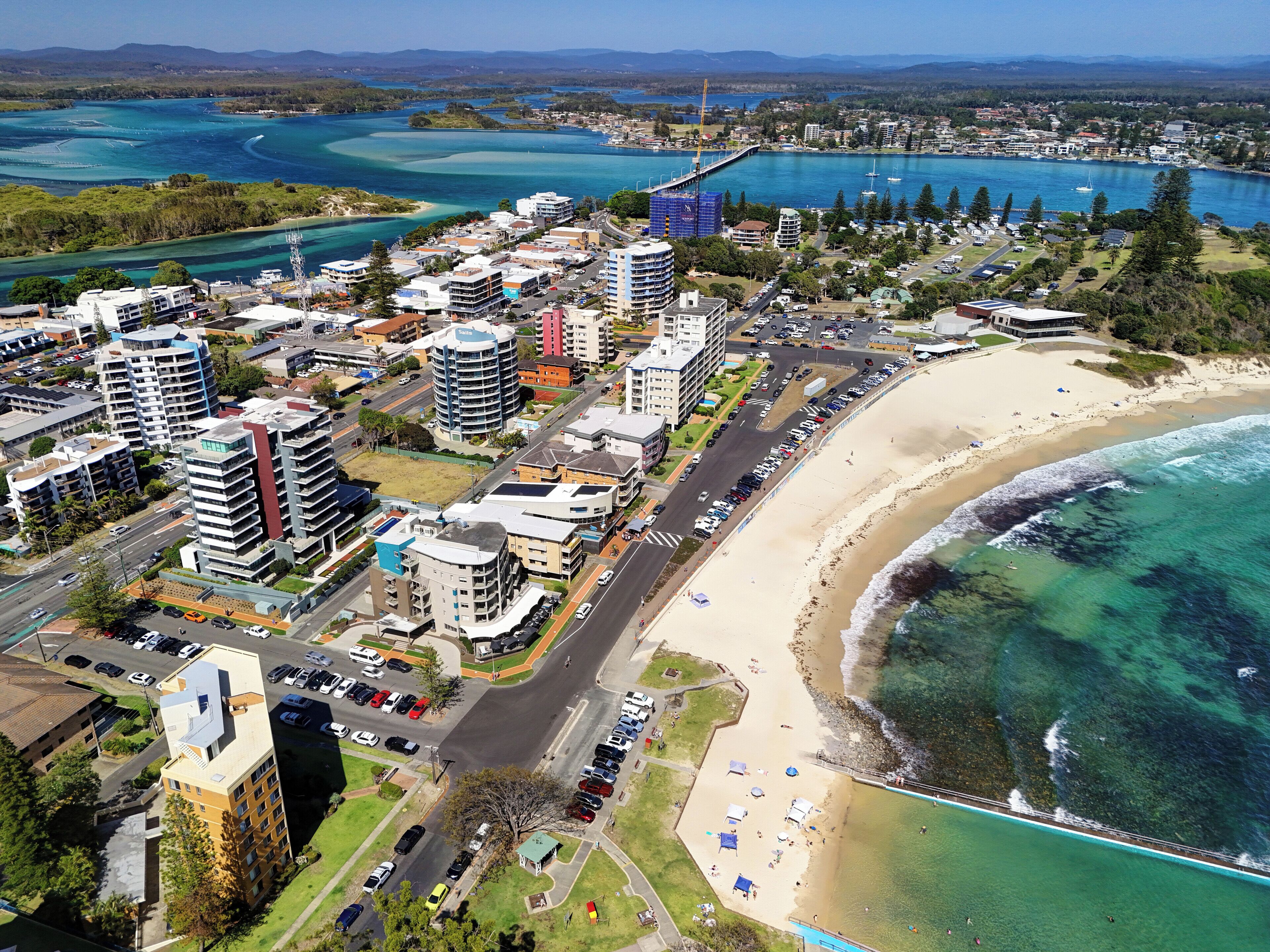 Un paisaje urbano costero con edificios altos, una playa y un puerto deportivo.