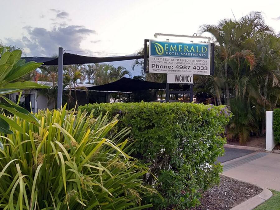 A motel sign for Emerald Motel Apartments with a vacancy notice, a phone number, and a directional arrow.