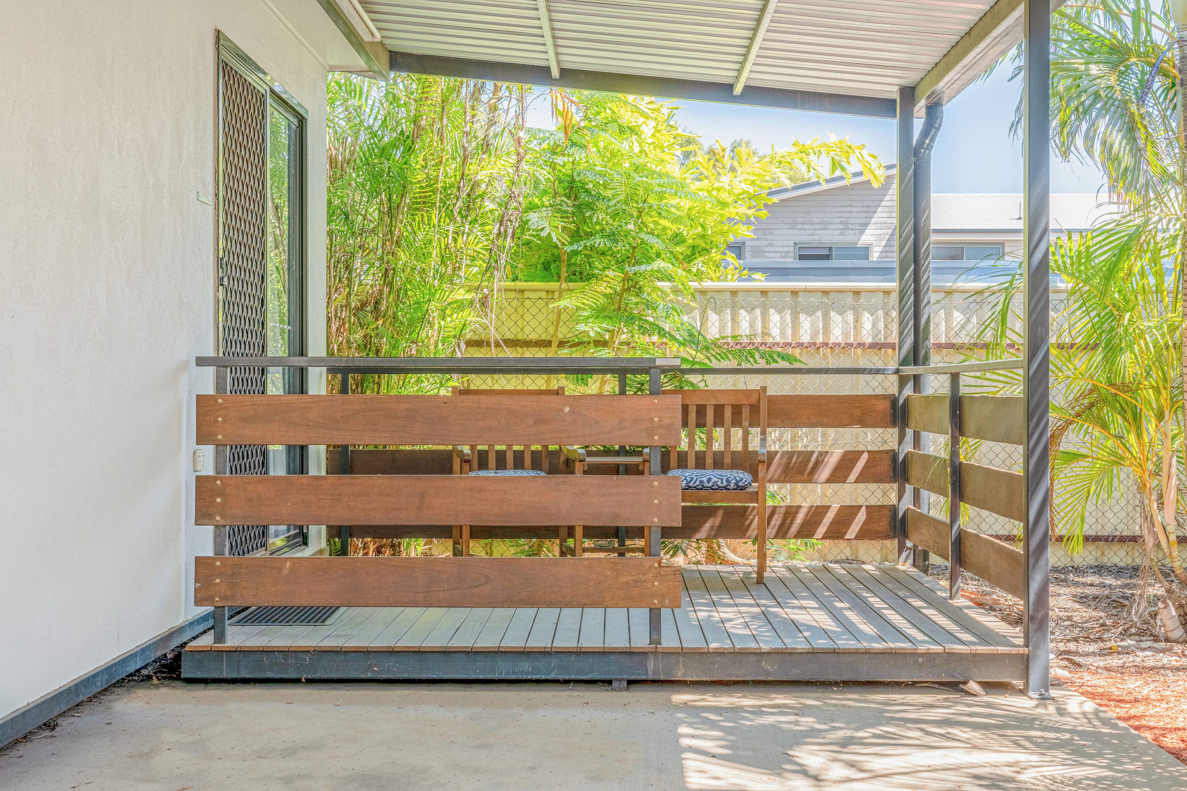 A wooden bench with a metal frame, a concrete floor, and a view of greenery and a building in the background.