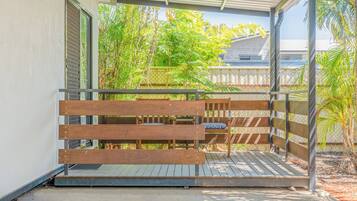 A wooden bench with a metal frame, a concrete floor, and a view of greenery and a building in the background.