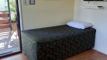 A single bed with a patterned bedspread, a wall-mounted TV, and a framed artwork with text.
