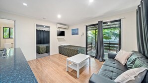 A modern living room with a sofa, a small table, a TV, and a balcony with curtains. - Emerald Motel Apartments (Emerald)