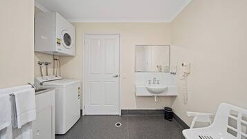 A small, clean bathroom with a washing machine, a sink, a mirror, and a white chair.