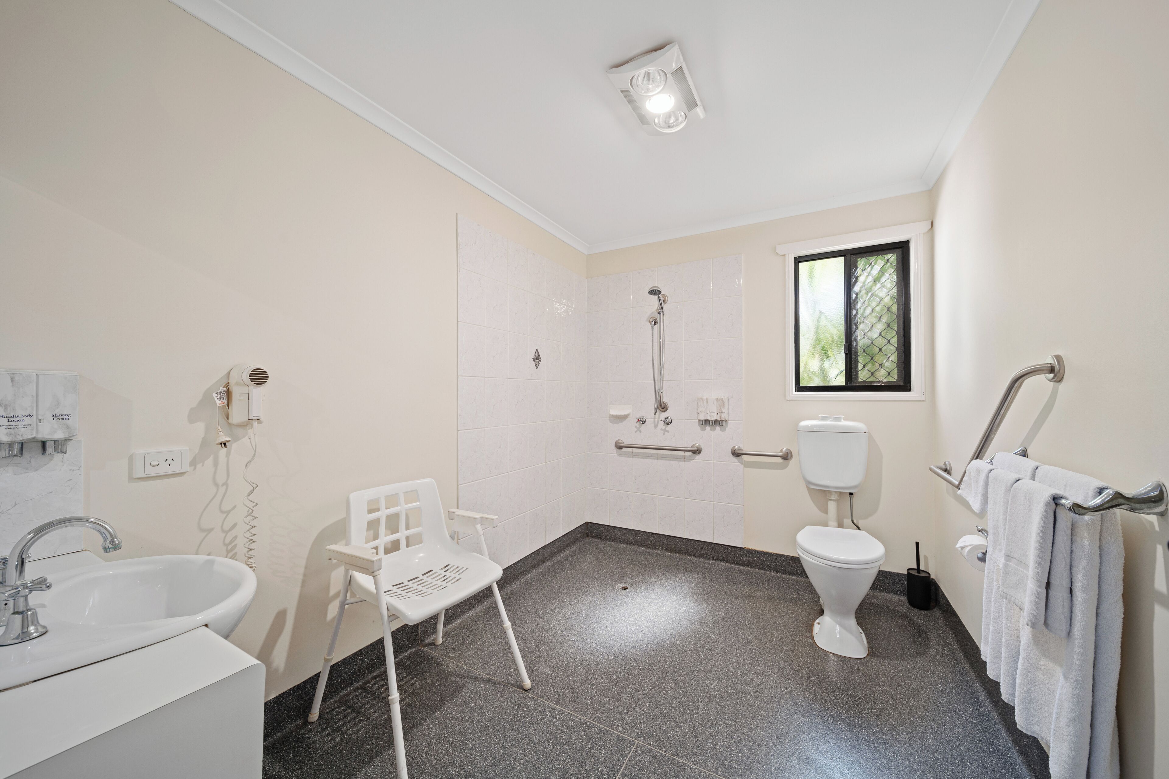 Une salle de bain équipée d’une douche, de toilettes, d’un lavabo et d’une chaise.
