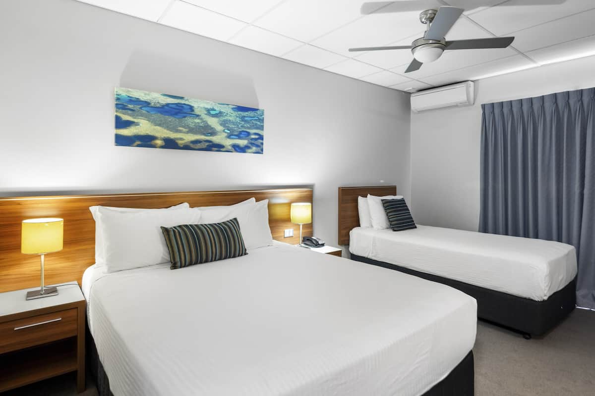 A hotel room with a large bed, a smaller bed, a ceiling fan, an air conditioning unit, and a painting on the wall.